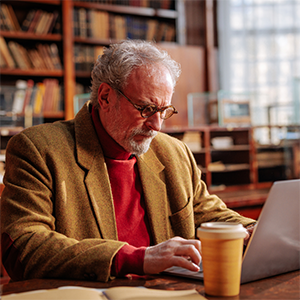 an elderly man types on his laptop in a library